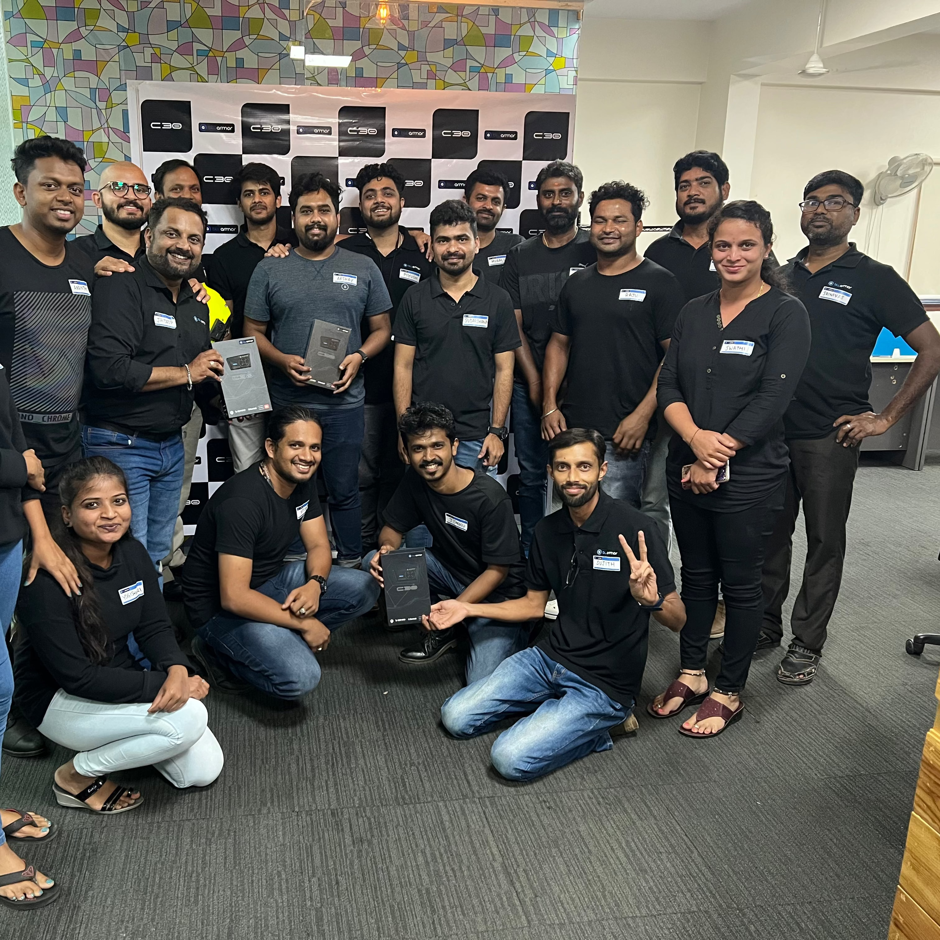 Group of people posing for a photo in an office setting with a colorful wall in the background.